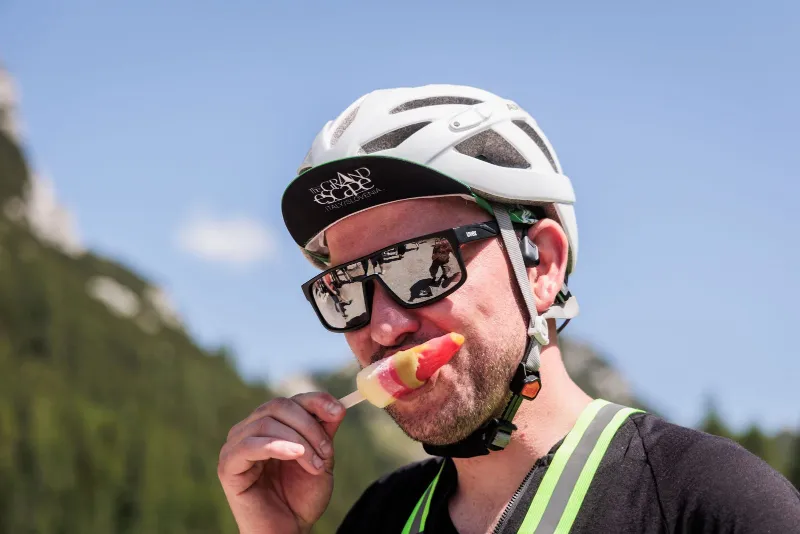 A rider in a helmet eating an ice lolly on a mountain stop