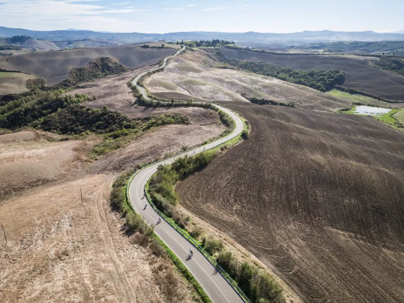 Riders on a winding road through the bare clay hills of the Crete Senesi