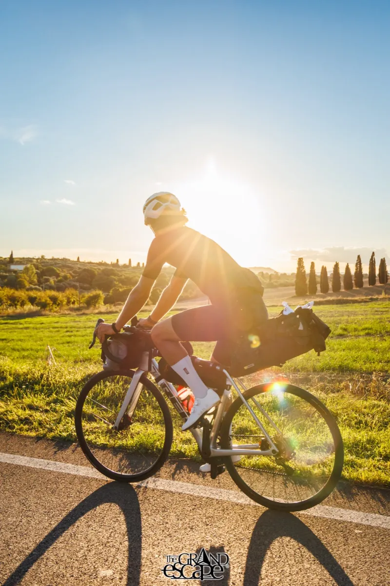 A rider with loaded bags in the low evening sun, cypresses behind